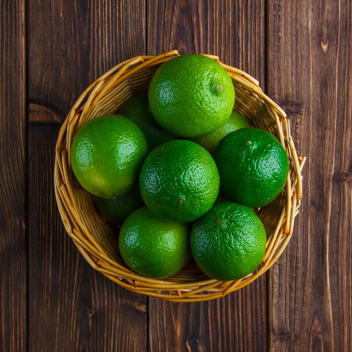 Limas frescas num cesto de vime, sobre uma mesa de madeira escura
